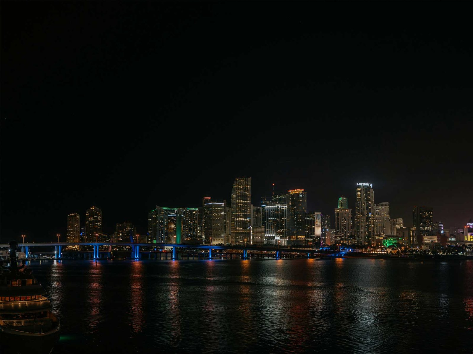 Downtown Miami skyline lit at night seen across Biscayne Bay, with the illuminated causeway in the foreground