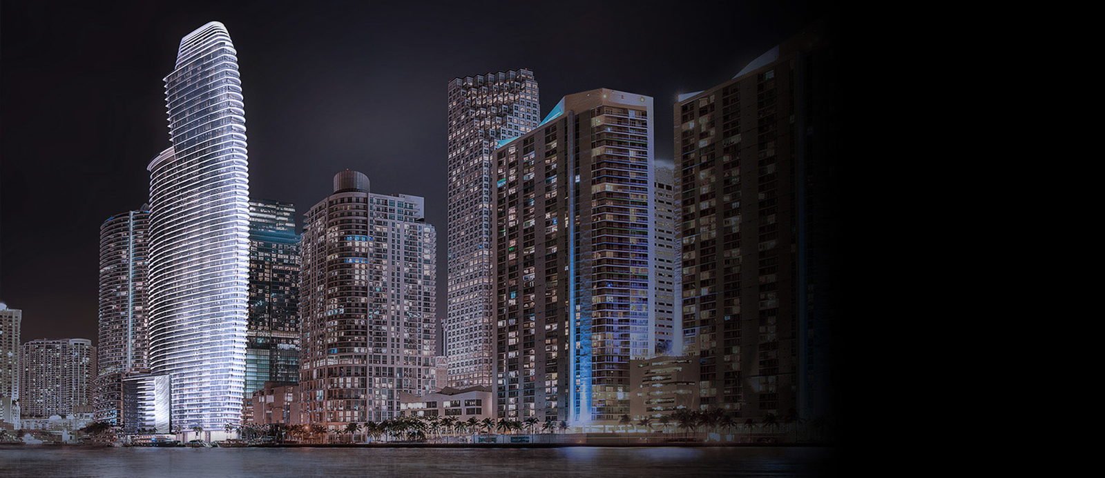 The tower lit at night within the Brickell skyline, seen across the water — developer rendering